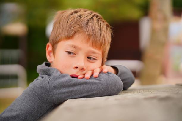 istock Young Caucasian boy sits on a bench, resting his head on his arm in a contemplative pose 1567168969