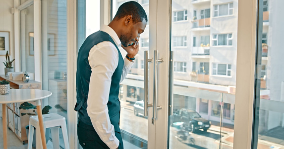 Black man, phone call and discussion in business by window for networking, deal or proposal at office. African businessman talking on mobile smartphone in conversation for communication at workplace