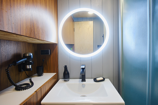 Round illuminated mirror over a white sink in a small bathroom