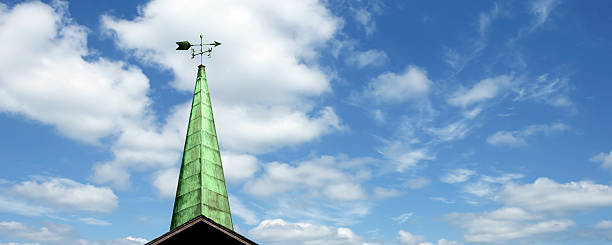 Weather vane above house with blue sky background. Copy space