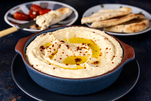 Homemade hummus with naan bread in the background. The Hummus is topped with olive oil and spices.