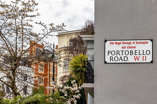 Portobello Road street sign on grey wall, with residential buildings and parks. Notting Hill, London, UK.