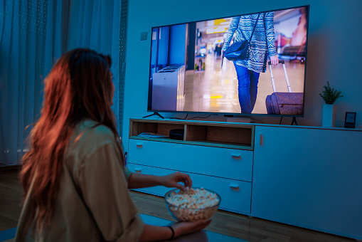 Young woman enjoying leisure time at home at night, watching a movie on TV and eating popcorn
