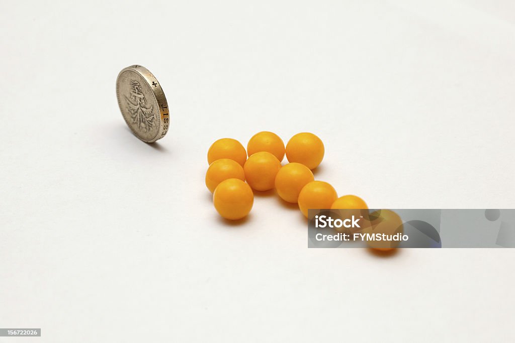 Yellow arrow of pills pointing on one pound coin Yellow arrow of pills pointing on one pound coin, isolated on white Arrow Symbol Stock Photo