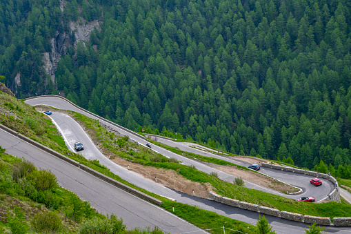 Alpine mountain road with cars driving through the hairpin corners along the Timmelsjoch high mountain pass during a beautiful springtime day in the Italian Alps of South Tirol.