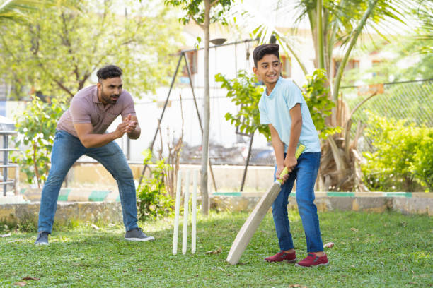 istock Cheerful indian father encouraging son from behind while playing cricket game at park - concept of Motivation, Guidance and parental support 1567229371