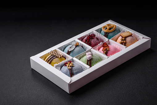 Delicious sweet colorful mochi desserts or ice cream with rice dough and toppings in a cardboard box on a dark concrete background