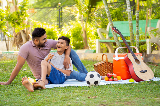 Happy indian father with son spending time together at picnic park during weekend holidays - concept of family bonding, Happy memories and outdoor fun