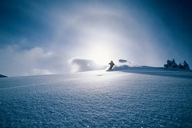 A skier has nothing but untracked powder with a sundog around the sun behind him.