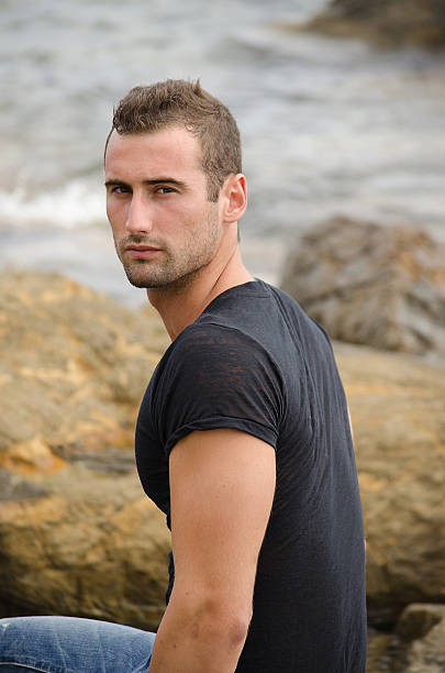 istock Handsome male model sitting on rock by the sea 156725032