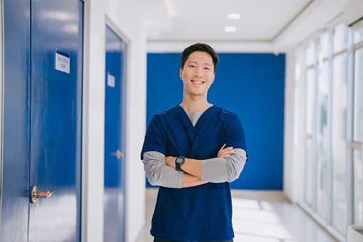 portrait asian male nurse looking at camera smiling standing in front of doctor's office