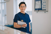 portrait asian male nurse looking at camera smiling standing in front of doctor's office