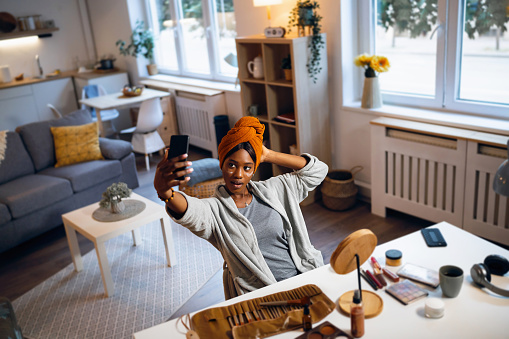 Young woman of Black ethnicity, taking selfie with mobile phone, while doing a skincare routine
