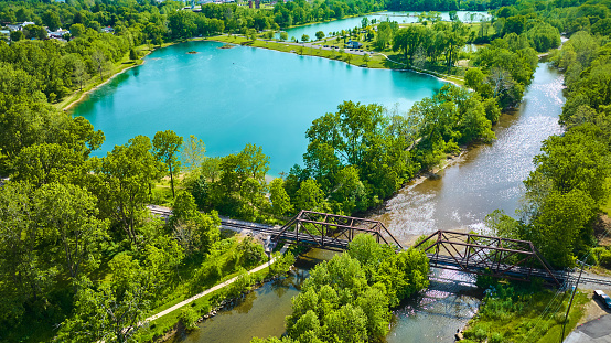 Image of Aerial beautiful teal blue pond with summertime trees and a river running under a train bridge
