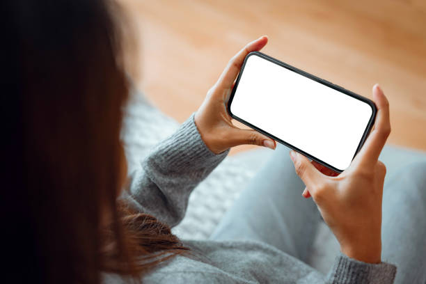 istock Closeup - Happy young woman holding mobile smartphone with blank white screen background while resting on the sofa in living room at home. Watching movies on the phone. 1567307599