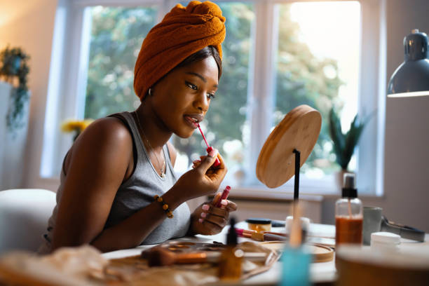 istock Woman of Black ethnicity applying a lip gloss, while doing her make up 1567309831