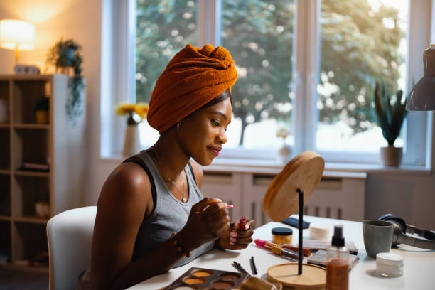 istock Woman of Black ethnicity applying a lip gloss, while doing her make up 1567310380