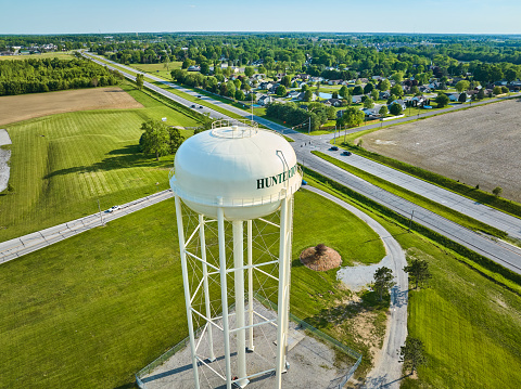 Image of Aerial green fields around white water tower with nearby civilization