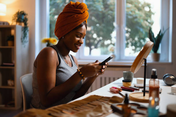 istock Woman of Black ethnicity using mobile phone while doing her make up 1567310387