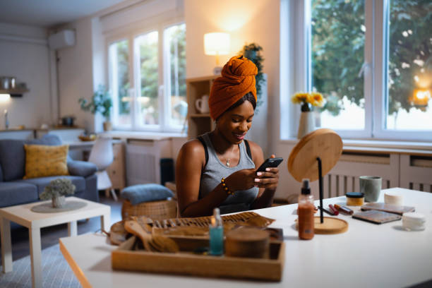 istock Woman of Black ethnicity using mobile phone while doing her make up 1567310390