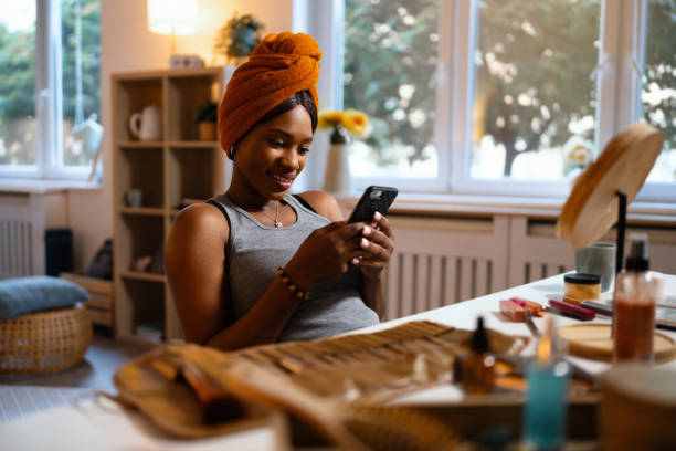 istock Woman of Black ethnicity using mobile phone while doing her make up 1567310415