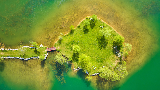 Image of Aerial over teal green pond with small island and land bridge leading to red walking bridge