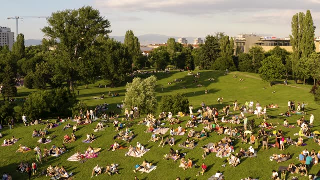 Crowd of people having good time on the grass in hot summer evening in a public park