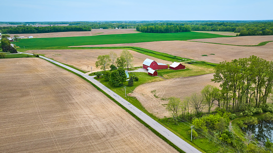 Image of Aerial red farmhouse with barn, shed, lake side property small forest landscaping empty fields asset