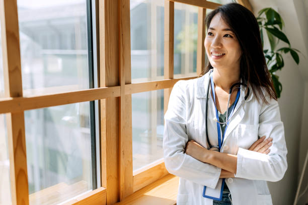 istock Smiling confident female doctor looking through window while standing near the window at modern office 1567331463