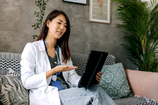 Smiling beautiful female doctor having video call on digital tablet while sitting on a sofa at small modern office stock photo