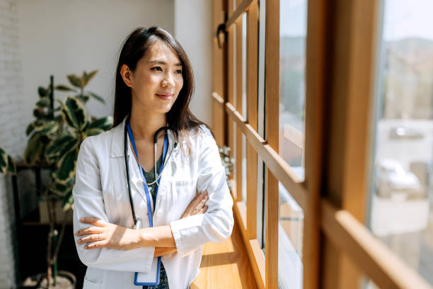 Smiling confident female doctor looking through window while standing near the window at modern office