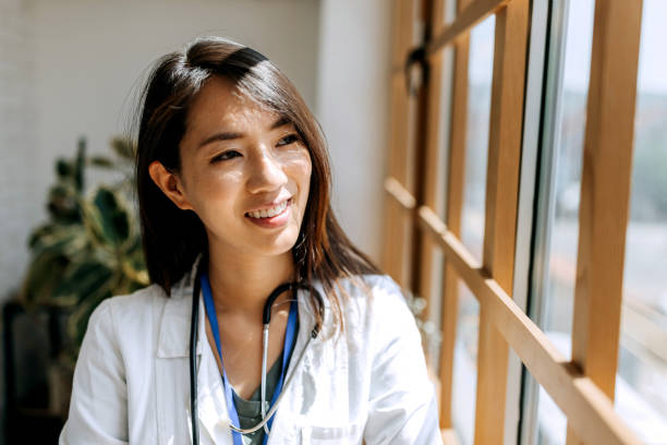 istock Smiling confident female doctor looking through window while standing near the window at modern office 1567332412