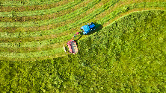 Image of Blue tractor mowing wavey line of tall grasses in downward aerial background asset