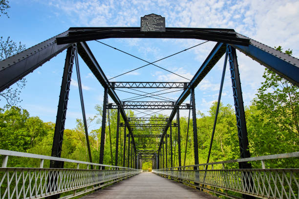 istock Bright blue sky with white clouds over black metal bridge, lush, green forest background 1567338233