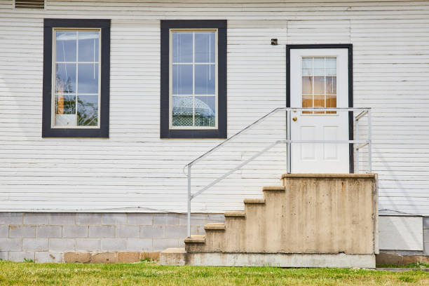 Image of Common whit house with white door and concrete steps and items crowding windows exterior