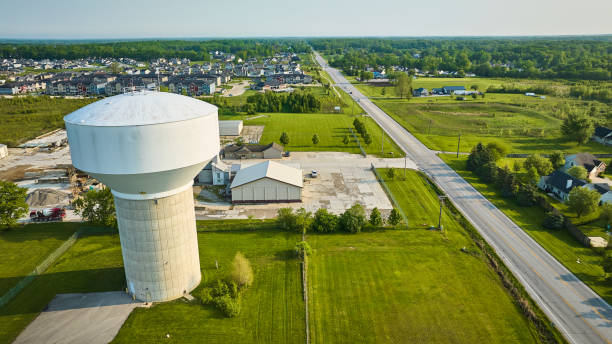 Construction near white nondescript water tower in rural area with distant homes, rental properties