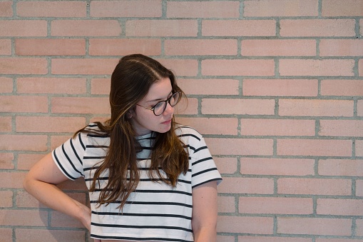 A young woman standing confidently in a black and white striped shirt against a brick wall