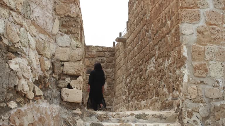 Woman in arabian black hijab walks upstairs in ruin ancient Fort Bahrain.