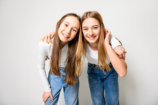 Twin girls sitting together outdoor portrait. Girls are preteen age, with long blond hair, dressed in casual spring weather fashion