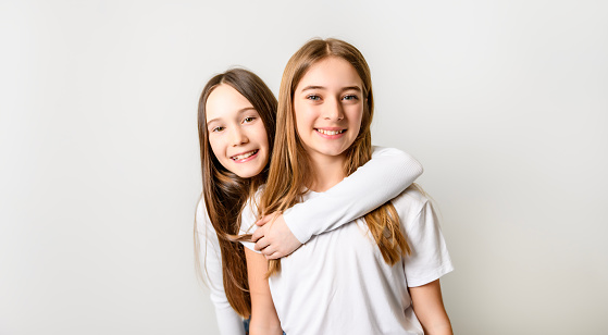 Headshot of two young girls toothy smiling at camera while hugging