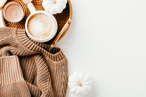 Knitted sweater with coffee cup, decorative pumpkins, rattan tray on white background. Autumn, fall, cozy home concept