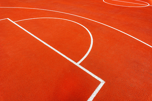 Minimalist abstract background of an orange tartan outdoor basketball court with white lines. Selective focus.