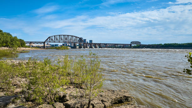 istock Distant truss arch bridge over Ohio River Louisville KY limestone shore, trees overlooking water 1567367192