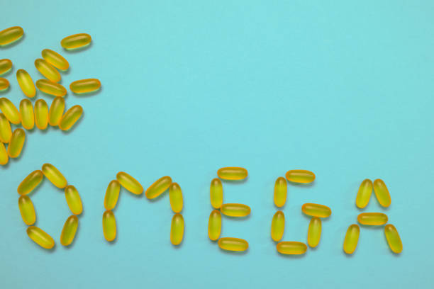 istock Pharmaceutical medicine capsules on blue background writes the text OMEGA. Pharmaceutical medicine capsules on blue background. Fish oil. Transparent fish oil on a blue background 1567389922