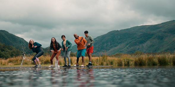 A wide angle view of a family skipping stones and playing riverside games together into a lake in Keswick inthe Lake District  They are on a staycation enjoying time together.