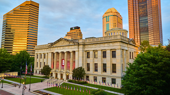 Image of Green lawn with flags outside Capital Square Foundation at sunrise with sun on skyscrapers aerial