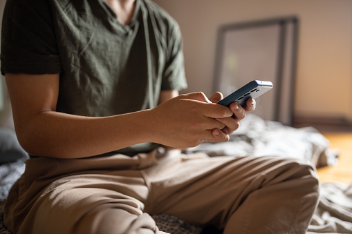 Young Chinese man using a smartphone in the bedroom of his house