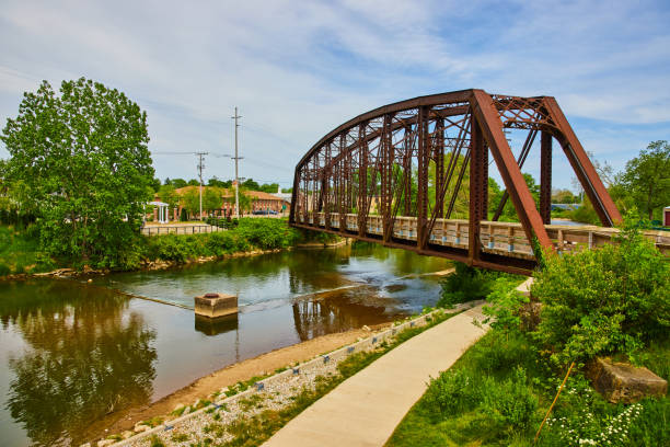 istock Green trees and shrubs on either side of river with iron truss bridge with sidewalk under bridge 1567397133