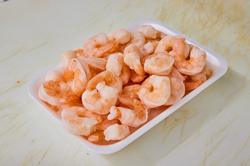 Image of Grocery store, meat department, pile pink cooked shrimp, seafood on white tray