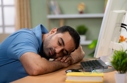 Tired Indian man sleeping on computer table at home - concept of resting, Stress relief and Overworked professional.